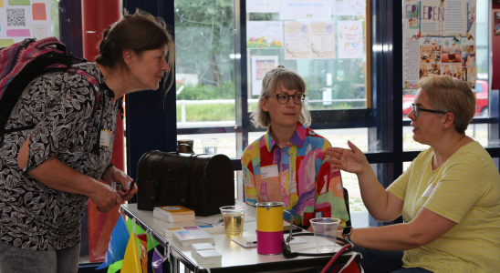 Ramona Hock und Diana Thiele (beide erweitereter Vorstand agsbb e.V.) sitzen am Tisch der agsbb und sprechen mit einem Mitglied.