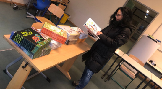 Min Tjoa-Schneider steht in einem großen Raum mit mehreren Tischen. Auf einem Tisch liegen mehrere Stapel Kinderbücher. Min blättert in einem der Bücher.