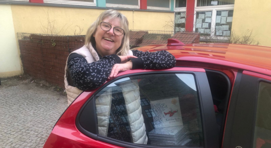 Simone Frübing steht an der hinteren Tür eines roten Autos. Kinderbücher liegen auf der Rückbank.